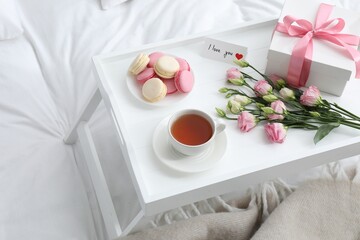Fototapeta na wymiar Tasty breakfast served in bed. Delicious macarons, tea, gift box, flowers and I Love You card on tray
