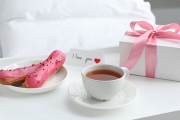 Tasty breakfast served in bed. Delicious eclairs, tea, gift box and I Love You card on tray