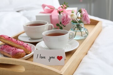 Tasty breakfast served in bed. Delicious eclairs, tea, gift box, flowers and card with phrase I Love You on tray