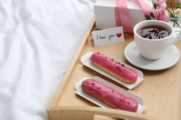 Tasty breakfast served in bed. Delicious eclairs, tea, gift box, flowers and card with phrase I Love You on tray