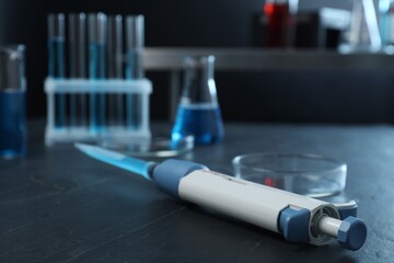 Laboratory analysis. Micropipette with liquid and petri dish on black table, closeup