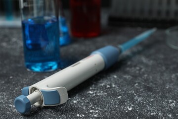 Laboratory analysis. Micropipette and beaker with liquid on grey table, closeup. Space for text