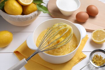 Delicious lemon curd in bowl, ingredients, whisk and sieve on white wooden table, closeup
