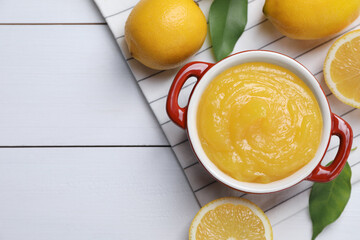Delicious lemon curd in bowl and fresh citrus fruits on white wooden table, flat lay. Space for text