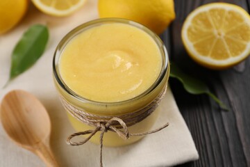 Delicious lemon curd in bowl, fresh citrus fruits and spoon on wooden table, closeup