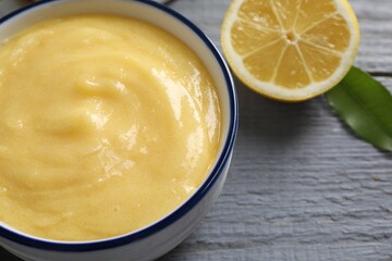 Delicious lemon curd in bowl, fresh citrus fruit and green leaf on grey wooden table, closeup