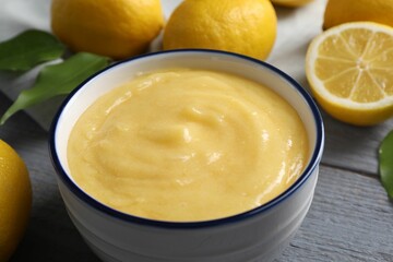 Delicious lemon curd in bowl, fresh citrus fruits and spoon on grey wooden table