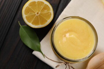 Delicious lemon curd in glass jar, fresh citrus fruit, green leaf and spoon on wooden table, top view