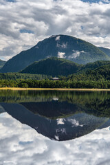 Summer reflections on the calm flat water at the Stangvikfjord with a view of the Søysetøran nature reserve and a farm in the mountains of Trollheimen, Møre og Romsdal Norway