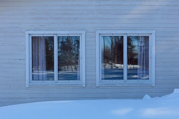 Two windows on a old wood building in winter with snow on the ground.