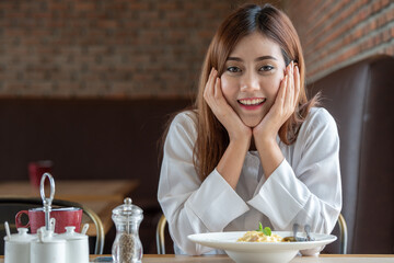 Woman in white clothes holding and smell white dish plate with pasta homemade spaghetti marinara in restaurant background. Lady smell and eat pasta spaghetti by fork.