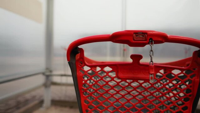 Take a close look at a red shopping cart with a coin already inserted, awaiting its journey through the aisles of the mall, with a blurred backdrop of shopping fervor