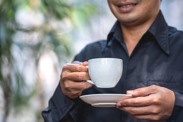 Asian man holding hot coffee in paper mug cup to sniff smell of espresso in morning sunlight. man...