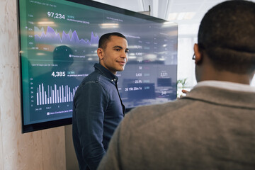 Young businessman presenting performance data to senior businessman on a large screen