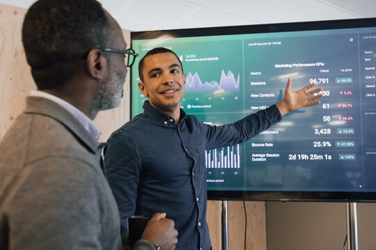 Young businessman presenting performance data to senior businessman on a large screen