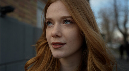 Portrait of young caucasian woman looking at the horizon in a vloudy city. Ginger hair. Freckled face.
