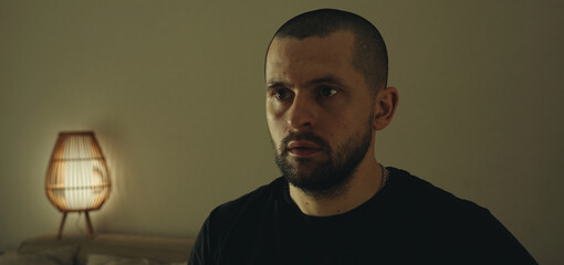 Indoor portrait of serious bearded man with looking astonished away sitting in his room. Peope and...