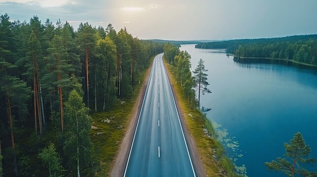 Aerial view of road with green woods by blue lakes water in summer Finland 