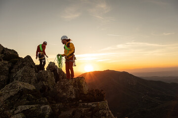 Two people are on a mountain, one of them is wearing a yellow jacket. The sun is setting in the...