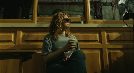 Happy young woman wearing sunglasses looking away sitting on the terrace of a cafe. Outside portrait of beautiful woman.