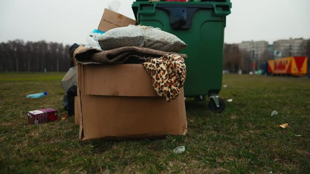 Cardboard boxes next to trash can in field with grass and trees