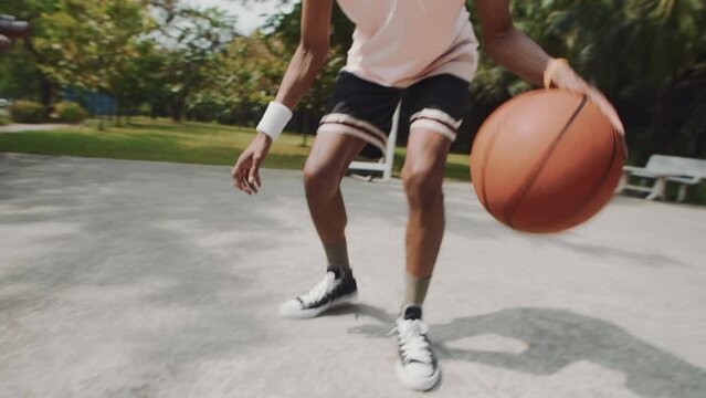 Handheld shot of black male player bouncing ball on floor during streetball game with friend on outdoor court