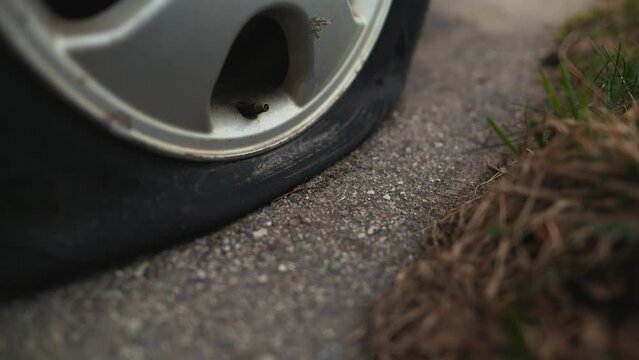 Close up of a flat tire on the roadside, showing tread and alloy wheel