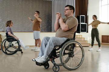 Selective focus shot of mature Caucasian man in wheelchair doing warm-up exercise during workout in...