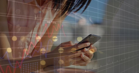 Image of multiple graphs with changing numbers, smiling biracial woman scrolling on cellphone