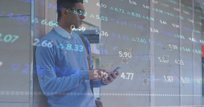 Image of multicolored trading board over biracial man standing and scrolling on smartphone