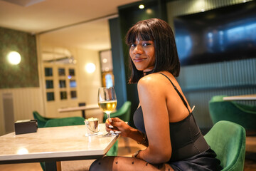African young woman drinking white wine in a glamorous bar