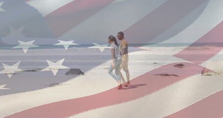 Fototapeta premium Image of american flag moving over couple holding hands and walking on beach