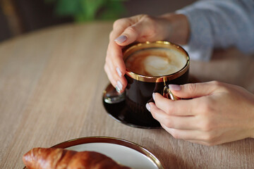 Close up of womans hands holding black cup of coffee. Morning coffee with croissant
