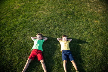 Picture of two brother having fun in the park, two cheerful children laying down on green grass, little boy and his friend playing outdoors, best friends, happy family, love and happiness concept