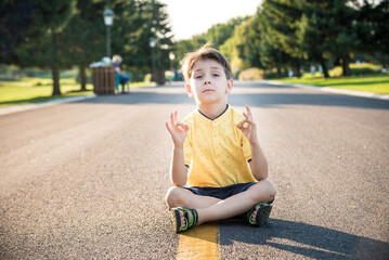 A boy is meditating sitting on the asphalt in the middle of the road. Spirit education relaxation concept