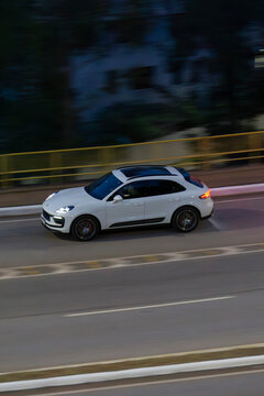  Panning shot of a white Porsche Macan GTS in urban area, Luxury SUV cruising during night time