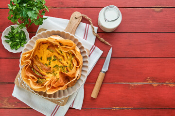 Homemade quiche or tart with slices of bacon and leeks with tortilla instead of dough on wooden cutting board on old red wooden background. Quiche open tart traditional French cuisine. Top view.