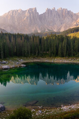 Adventurous person with arms raised on the shores of a lake surrounded by alpine trees and mountains. A sense of freedom. Lago di Carezza. Dolomites. Italy