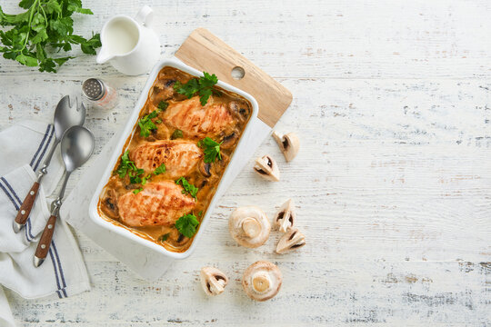 Baked chicken breast bbq with mushrooms and garlic in cream sauce on white wooden table backgrounds. Top view image with ingredients for cooking. Top view with copy space.