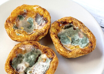 Close-up of the bakery with green mold on a light plate. Dangerous microorganisms.