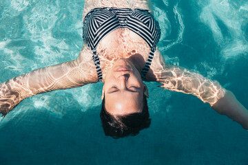 A woman is swimming in a pool she is with her eyes closed, the water is clear and calm
