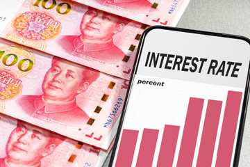 Mobile phone showing interest rate text near yuan banknotes. Rising inflation, growth interest rate in China.