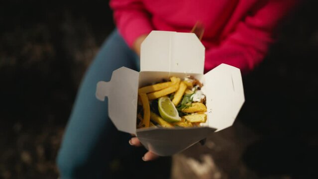 Woman in pink sweater holding box of French fries, fast food indulgence