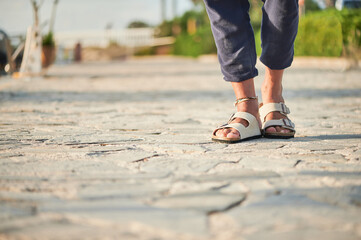 Legs of an unrecognizable trendy man walking with comfortable sandals on his feet on the pier of...