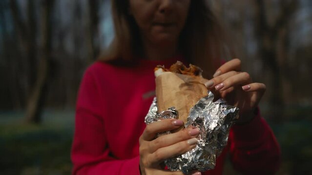 A woman enjoys a burrito wrapped in foil while sitting at a fun event