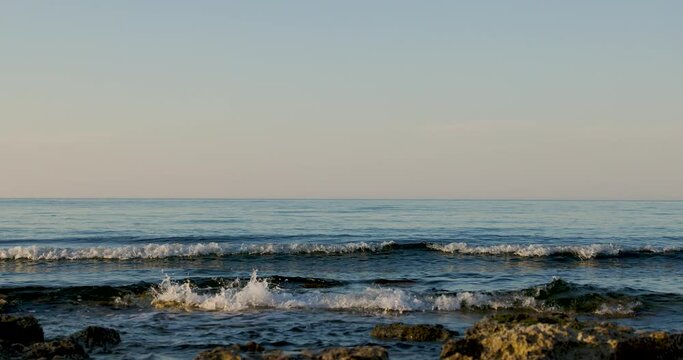 Onde in riva al mare in primo piano con mare calmo e bassa marea 
