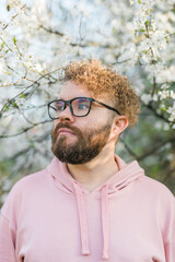 Man with beard and mustache on smiling face near sakura flowers or blooming spring tree. Soft and gentle concept. Bearded man with stylish haircut with flowers on background, close up. Hipster near