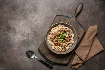 Risotto with mushrooms in a plate on a wooden cutting board, dark grunge background. Italian traditional dish. Top view, flat lay, copy space.