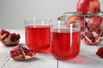 Tasty pomegranate juice in glasses and fresh fruits on white tiled table