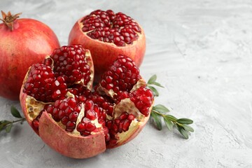 Fresh pomegranates and green leaves on grey textured table, closeup. Space for text